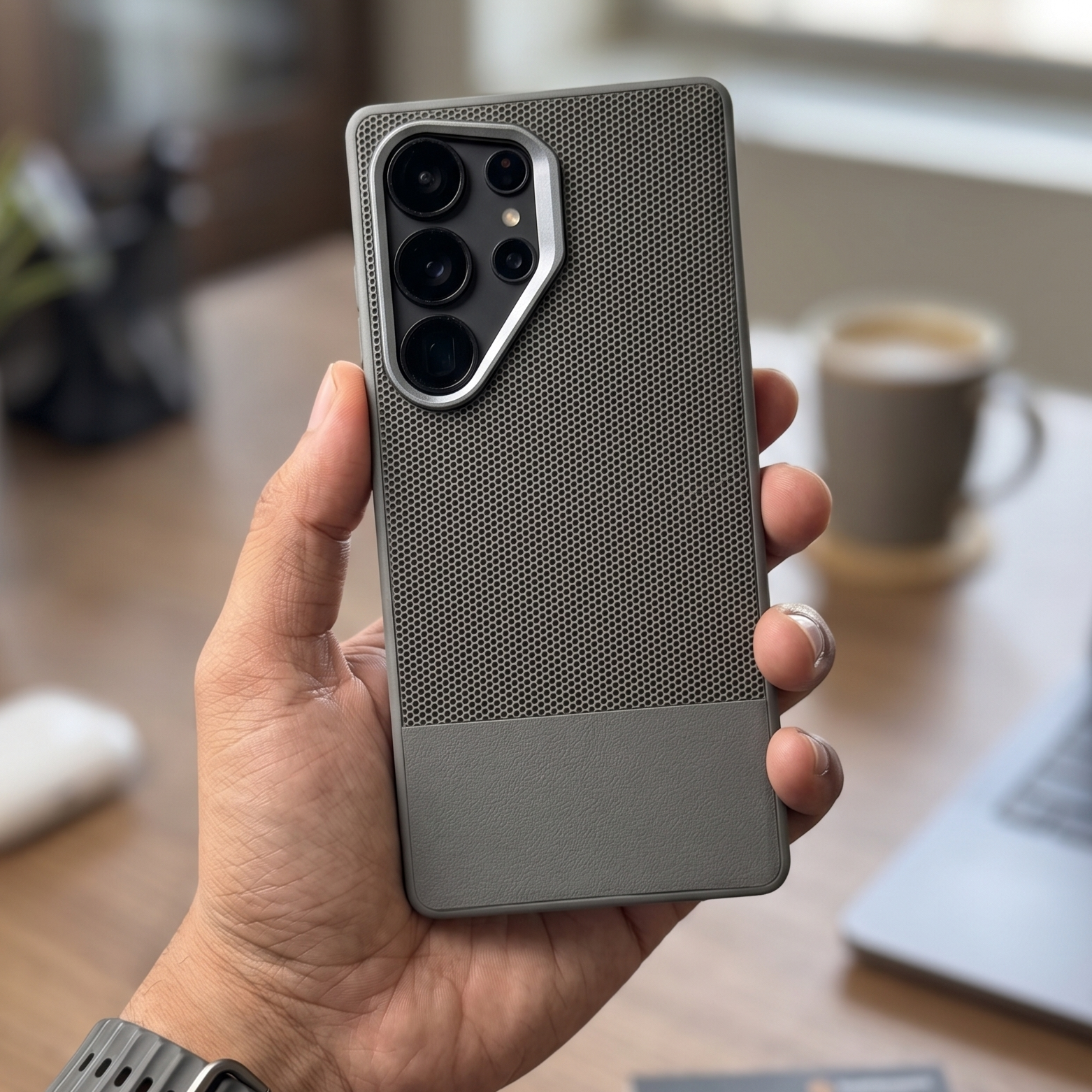 Hand holding a smartphone with a textured case on a blurred indoor background