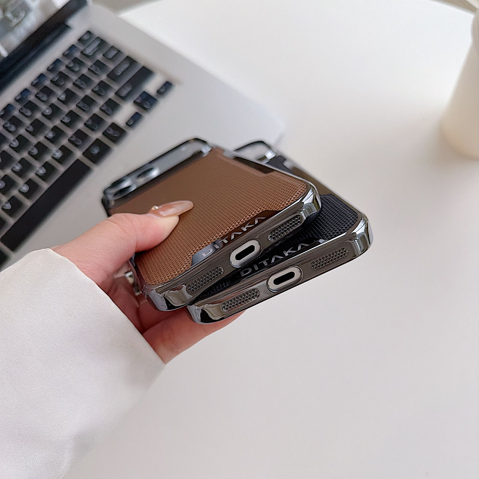 Person holding a phone case with a laptop in the background